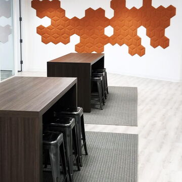 Modern Office Break Area with Hexagonal Wall Accents and Wooden Bar Tables