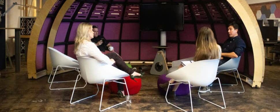 Four People Having a Discussion in a Modern Office Lounge with Unique Curved Architecture and Vibrant Colors