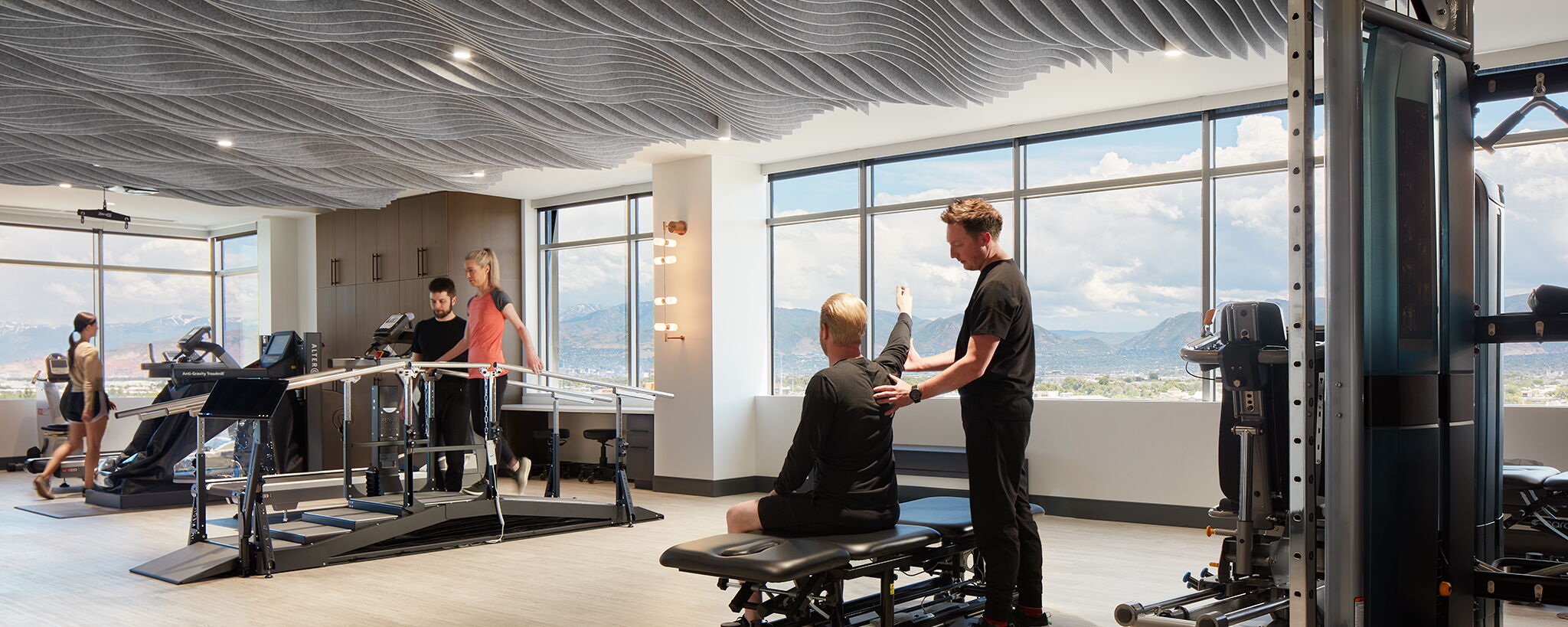 Modern Gym Facility with Clients Using Equipment and Trainer Assisting a Client